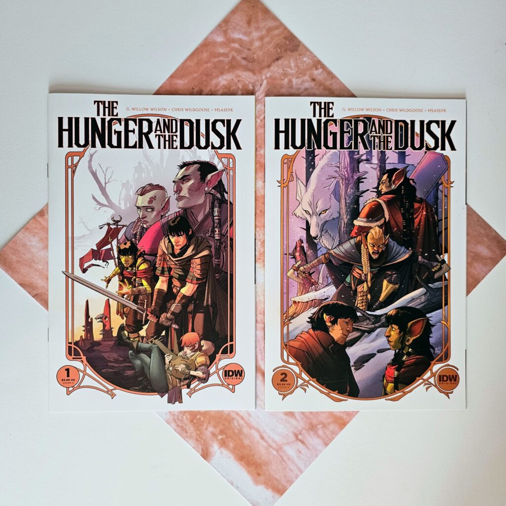 Issues 1 and 2 of The Hunger and The Dusk laying on a square piece of paper that looks like pink marble.